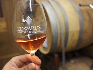Winemaker holding glass of our Rosé with barrels in the background